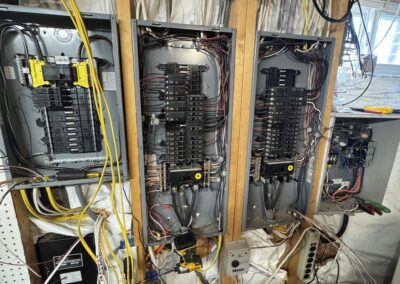 A basement electrical setup with three breaker boxes mounted on a wood frame, surrounded by numerous wires. A note on a clipboard is visible in the foreground.
